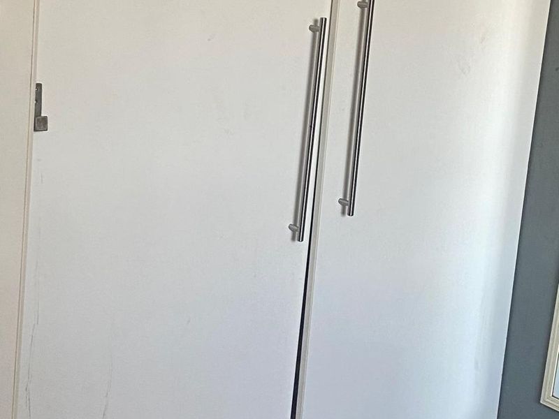 A close-up view of built-in bedroom cupboards featuring white doors with modern metal handles, showing signs of surface wear and scuffing.