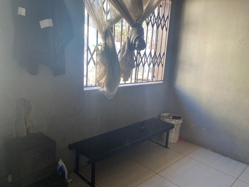 A bedroom space featuring tiled flooring and a window with a security gate, currently showing signs of wear and requiring maintenance.