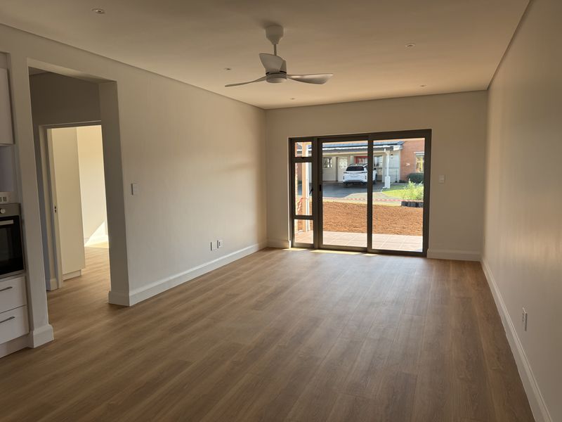 Spacious open-plan living area featuring modern laminate flooring, recessed lighting, a ceiling fan, and direct access to the exterior through sliding glass doors.