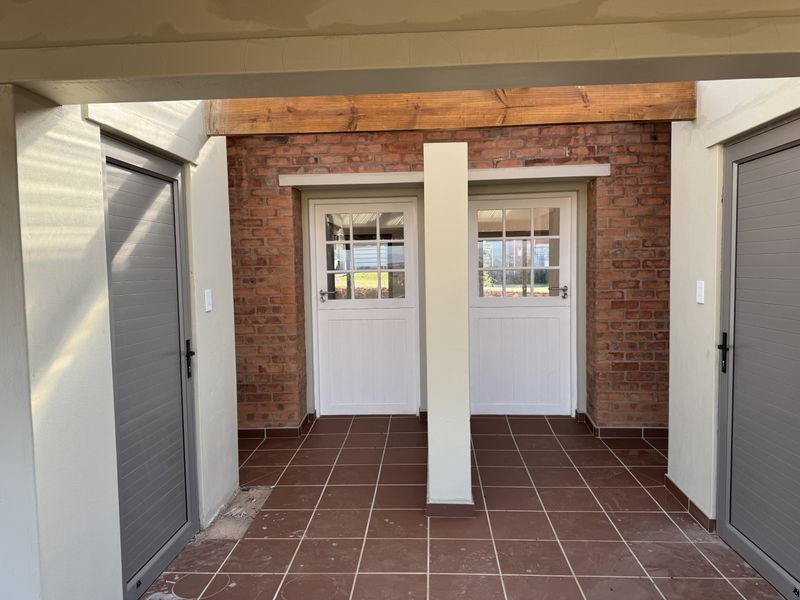 A covered patio area featuring exposed brickwork, tiled flooring, and multiple access points with stable-style and aluminium doors.