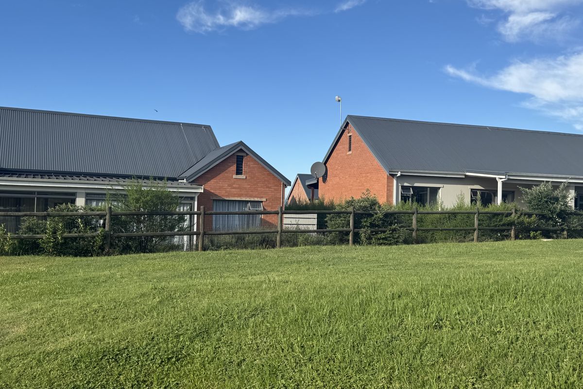 Rear view of the townhouse complex featuring brick facades, corrugated metal roofing, and a shared lawn area enclosed by a timber fence.