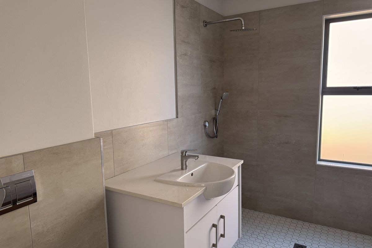 Modern bathroom featuring a vanity with basin, wall-mounted shower fixtures, and neutral tiled finishes.