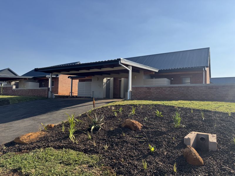 Front exterior view of a modern townhouse featuring a brick facade, metal roofing, and a covered carport with a landscaped front garden.