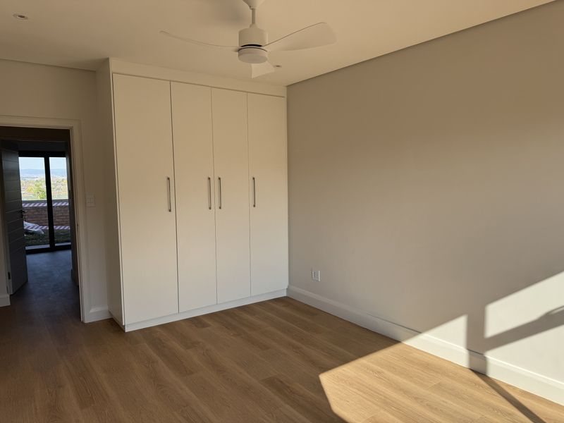 A bright, modern bedroom featuring neutral walls, light laminate flooring, and ample built-in cupboard storage with a ceiling fan.