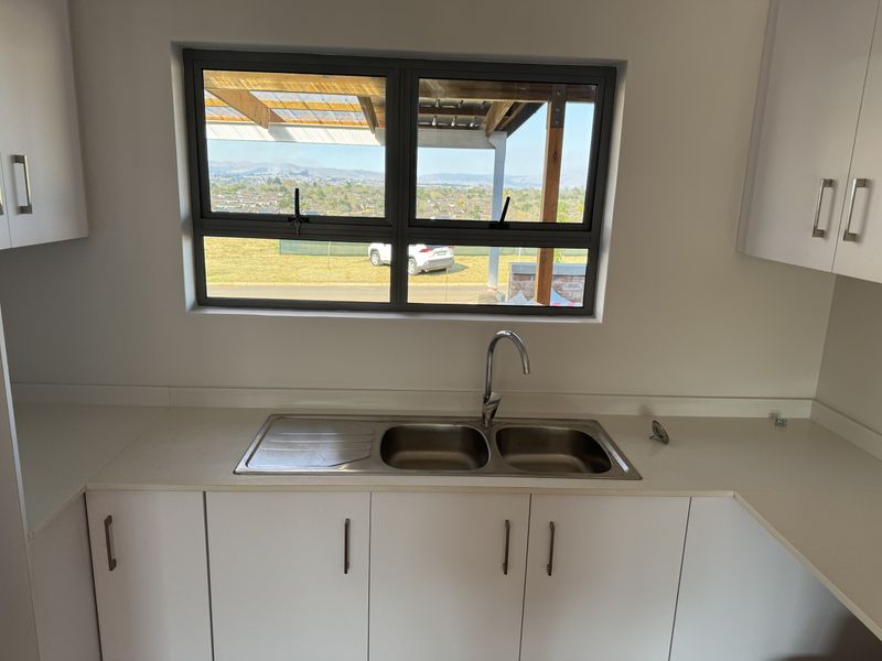 A clean, modern kitchen area featuring white cabinetry, a double bowl stainless steel sink, and a window with scenic views.