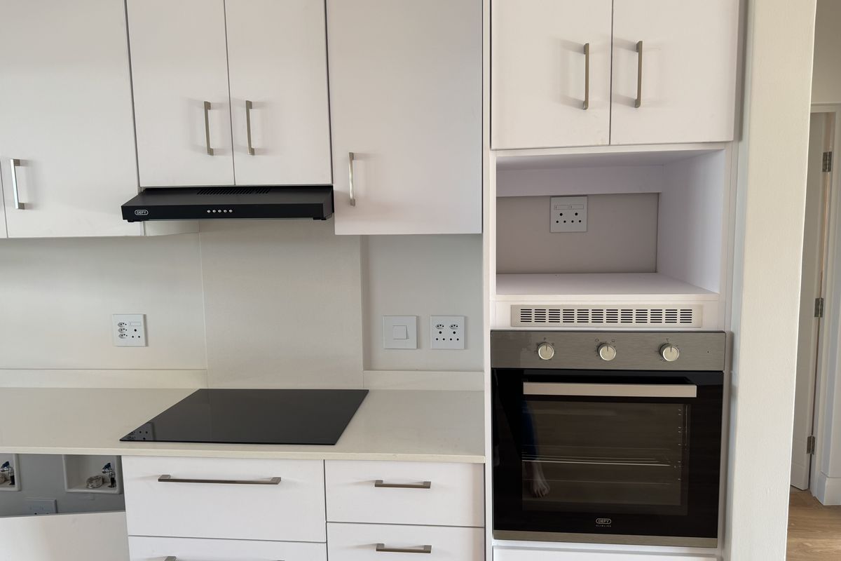 Modern kitchen featuring white cabinetry, stone countertops, a built-in oven, electric hob, and an integrated extractor fan.