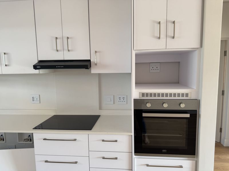 Modern kitchen featuring white cabinetry, stone countertops, a built-in oven, electric hob, and an integrated extractor fan.