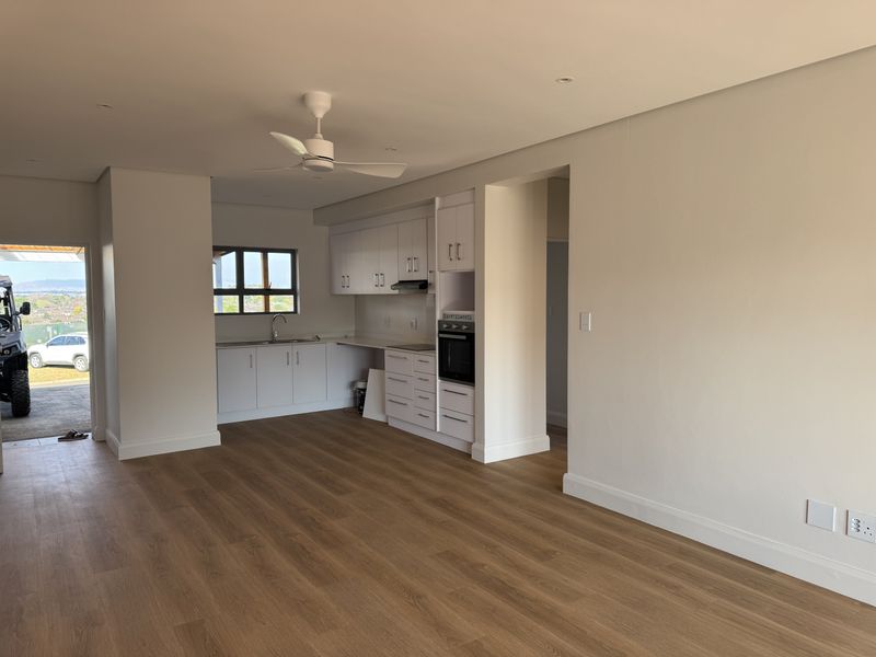Modern open-plan kitchen and living area featuring white cabinetry, integrated appliances, wood-look laminate flooring, and a ceiling fan in a bright, neutral space.