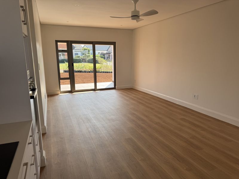 Bright open-plan living area featuring modern laminate flooring, a ceiling fan, and large sliding glass doors leading to an outdoor space.