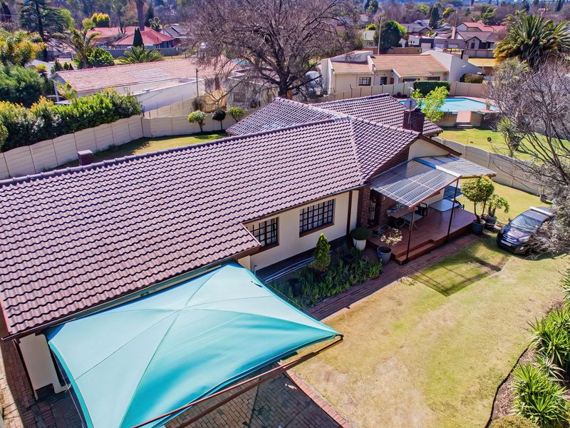 Aerial view of the property featuring a tiled roof, covered patio area, landscaped garden, and paved driveway within a residential neighborhood.