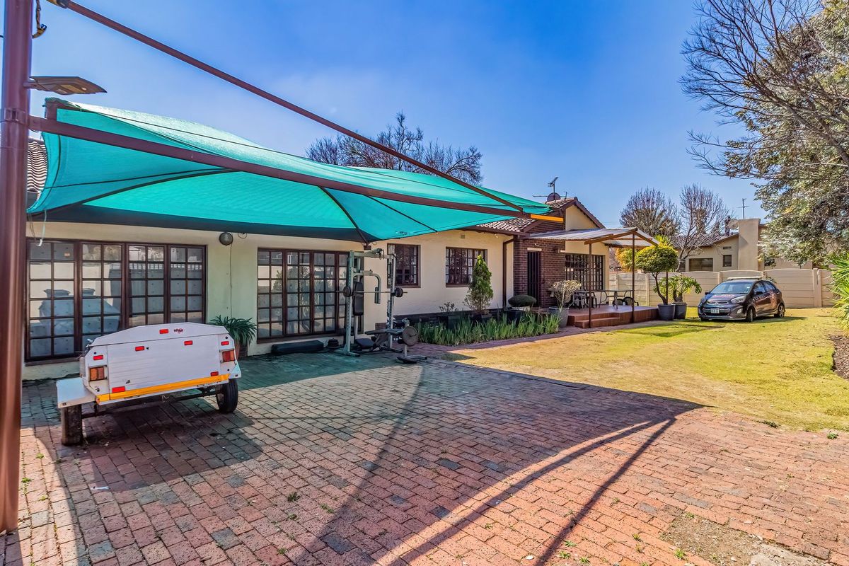 Rear exterior view featuring a brick paved area with a large shade sail, a well-maintained lawn, and a small timber deck.