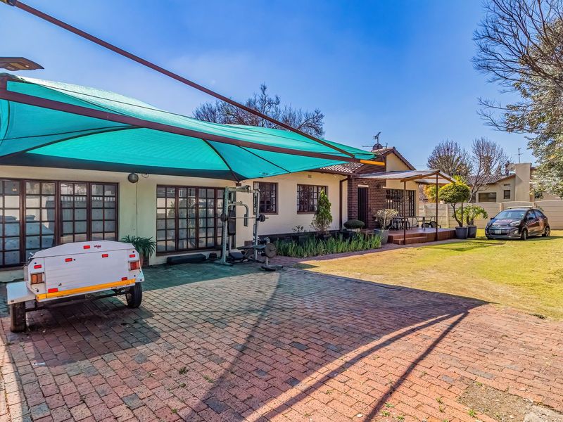 Rear exterior view featuring a brick paved area with a large shade sail, a well-maintained lawn, and a small timber deck.