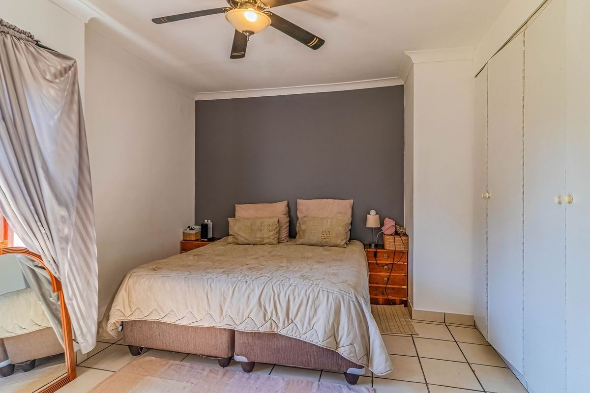 A bedroom featuring tiled flooring, a ceiling fan, and built-in cupboards with a neutral grey feature wall.