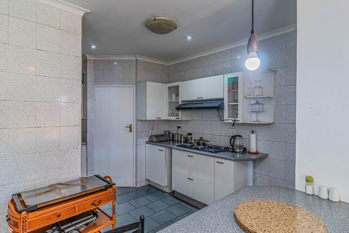 A functional kitchen featuring built-in cabinetry, a gas hob with extractor fan, tiled splashbacks, and durable floor tiles.