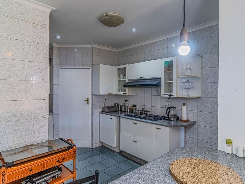 A functional kitchen featuring built-in cabinetry, a gas hob with extractor fan, tiled splashbacks, and durable floor tiles.