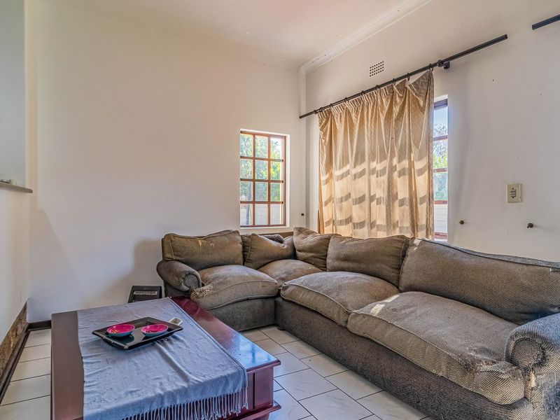 A living room featuring tiled flooring, natural light from windows, and direct access to the garden area.