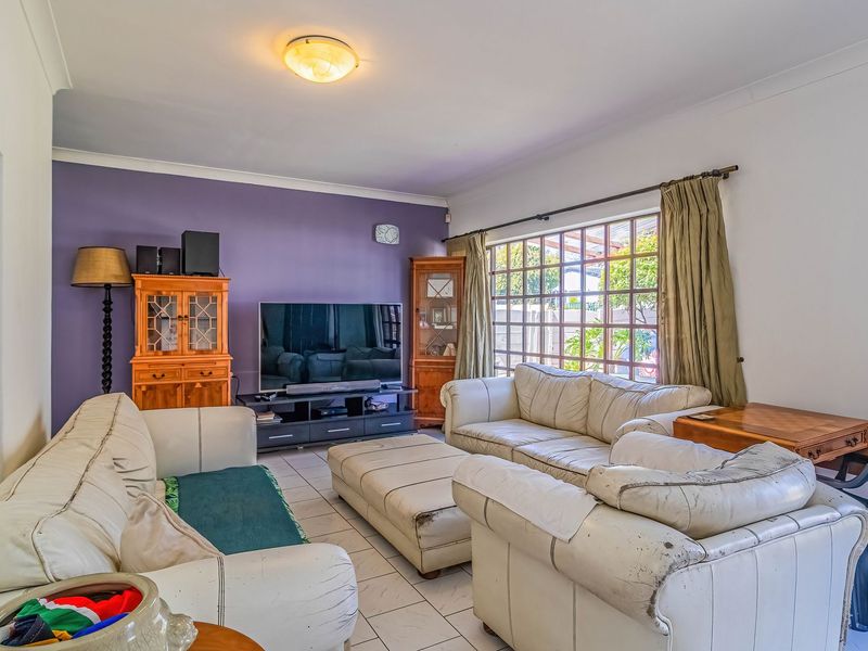 A spacious living room featuring tiled flooring, a large window with a grid pattern, and a feature wall, offering a comfortable living space.