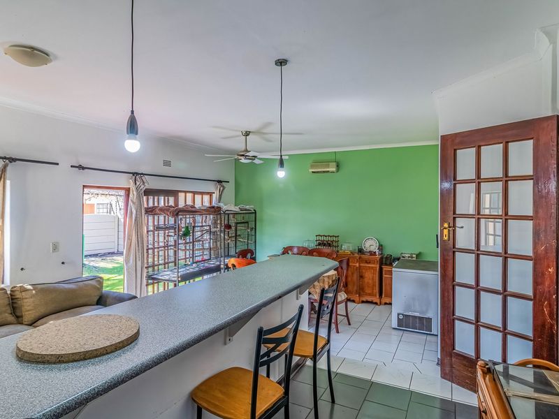 Open-plan living and dining area featuring a breakfast bar, tiled flooring, ceiling fan, and direct access to the rear garden through a glass door.
