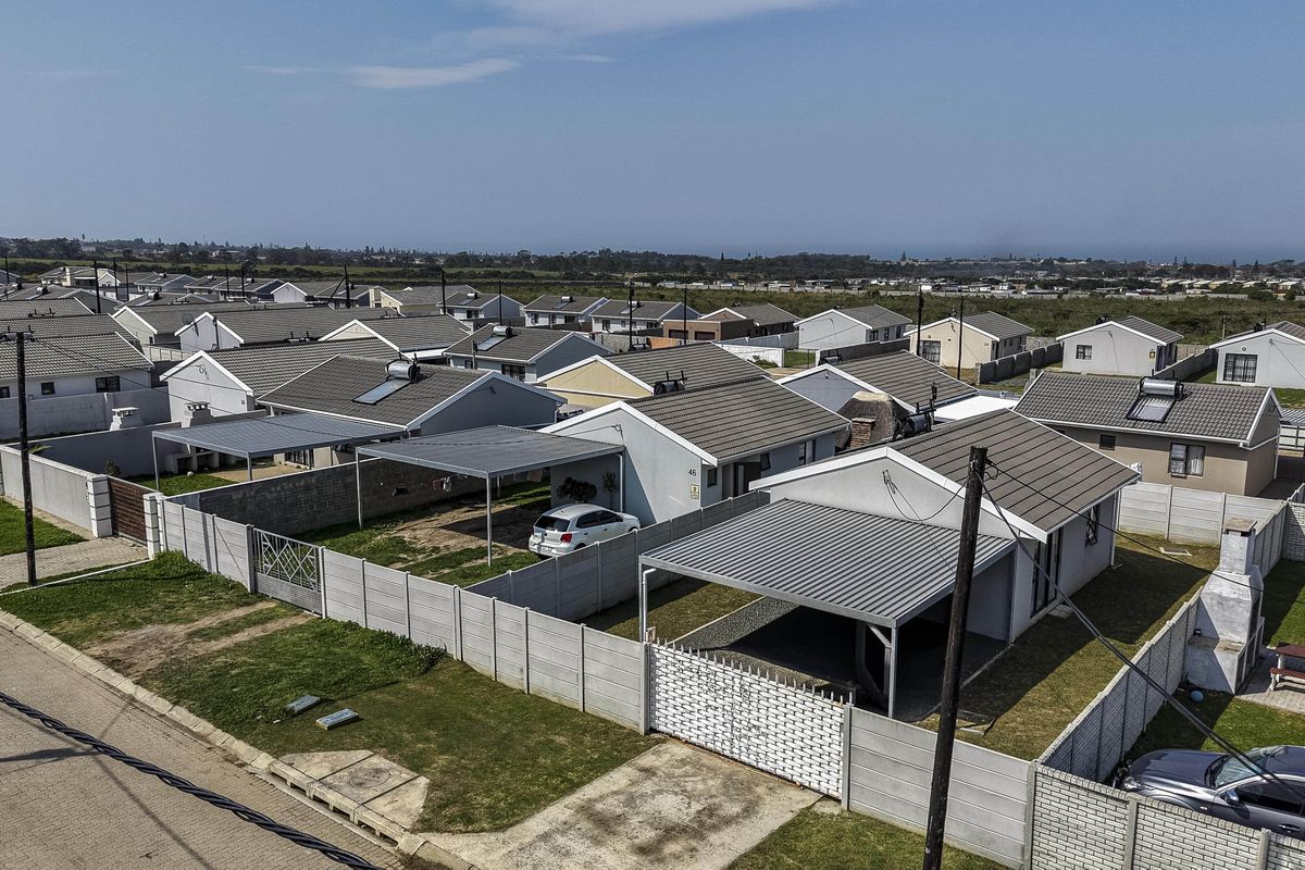 Aerial view of a residential estate featuring detached houses with tiled roofs, metal carports, and enclosed garden areas with boundary walls.