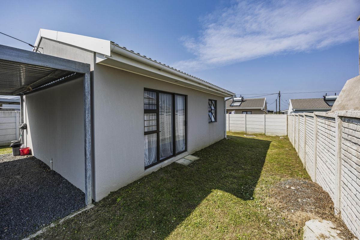 Rear view of the property featuring a carport, gravel driveway, and a private garden enclosed by precast concrete boundary walls.