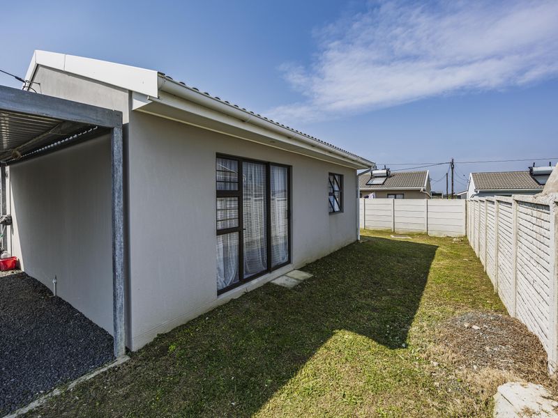 Rear view of the property featuring a carport, gravel driveway, and a private garden enclosed by precast concrete boundary walls.