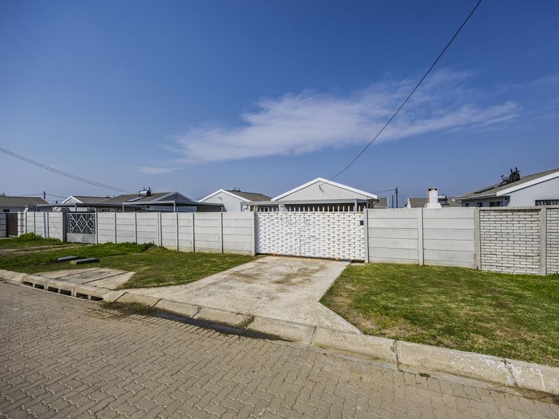 Front view of the property featuring a concrete boundary wall, metal driveway gate, and paved street access.