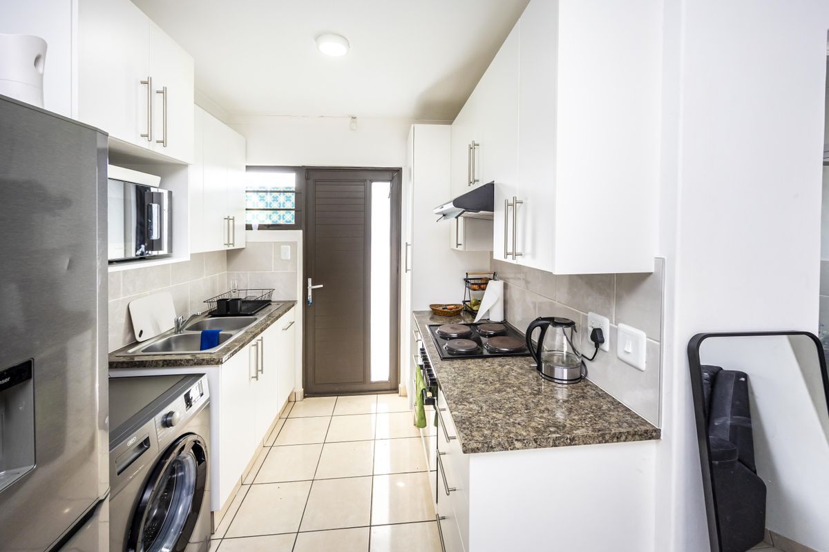 A functional galley-style kitchen featuring white cabinetry, granite-look laminate countertops, a built-in electric hob, and tiled flooring with direct access to the exterior.