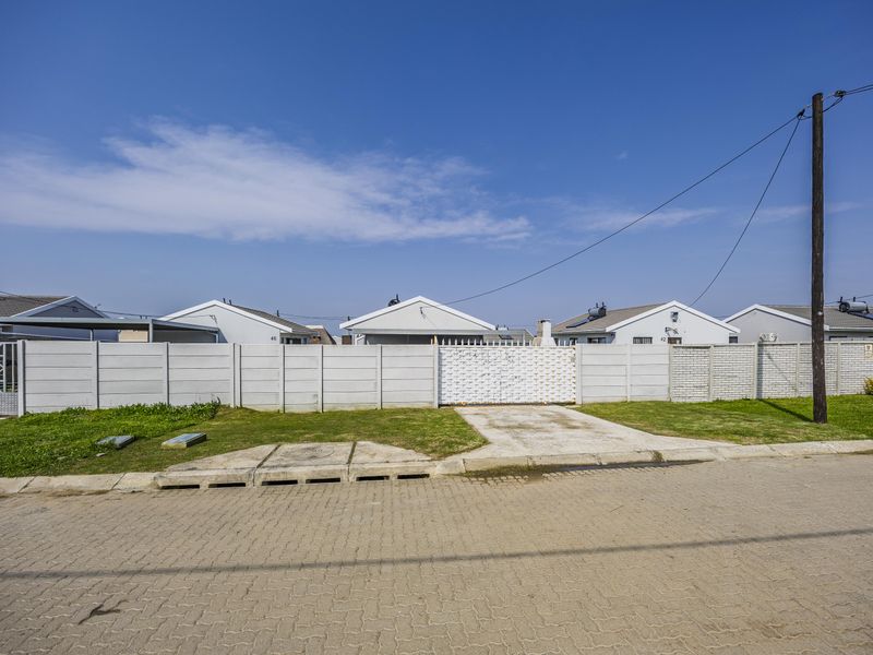 Front view of the property featuring a paved driveway, secure metal gate, and precast concrete boundary walling.