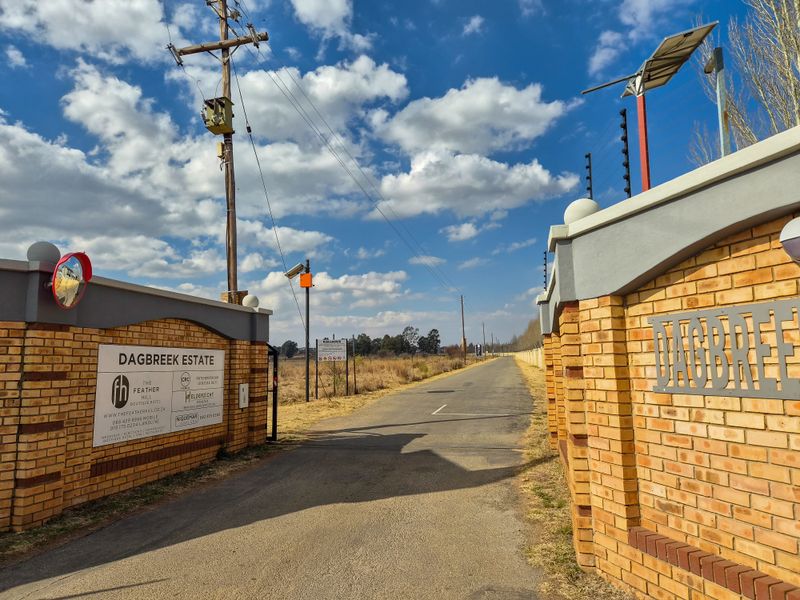 Entrance view of Dagbreek Estate featuring a brick boundary wall, electric fencing, and an asphalt driveway leading into the property.