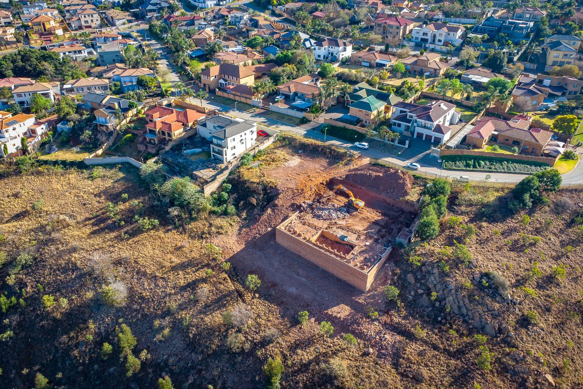 Aerial view of a residential vacant land plot featuring an excavated foundation and ongoing site preparation work within an established suburban neighborhood.