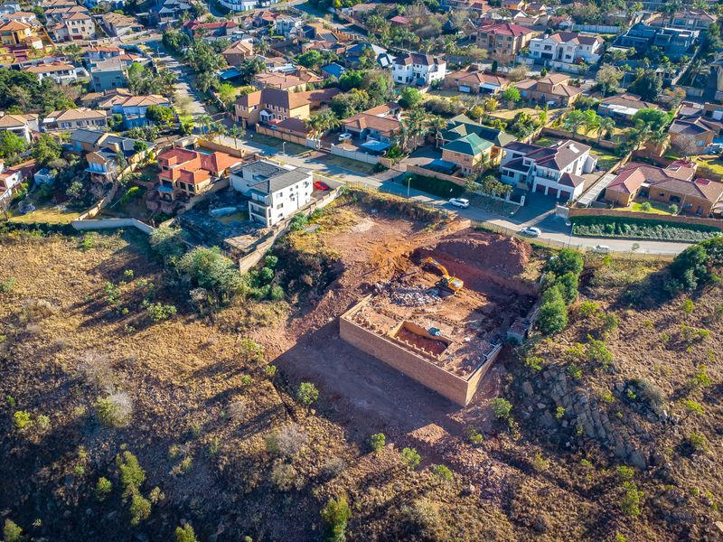 Aerial view of a residential vacant land plot featuring an excavated foundation and ongoing site preparation work within an established suburban neighborhood.