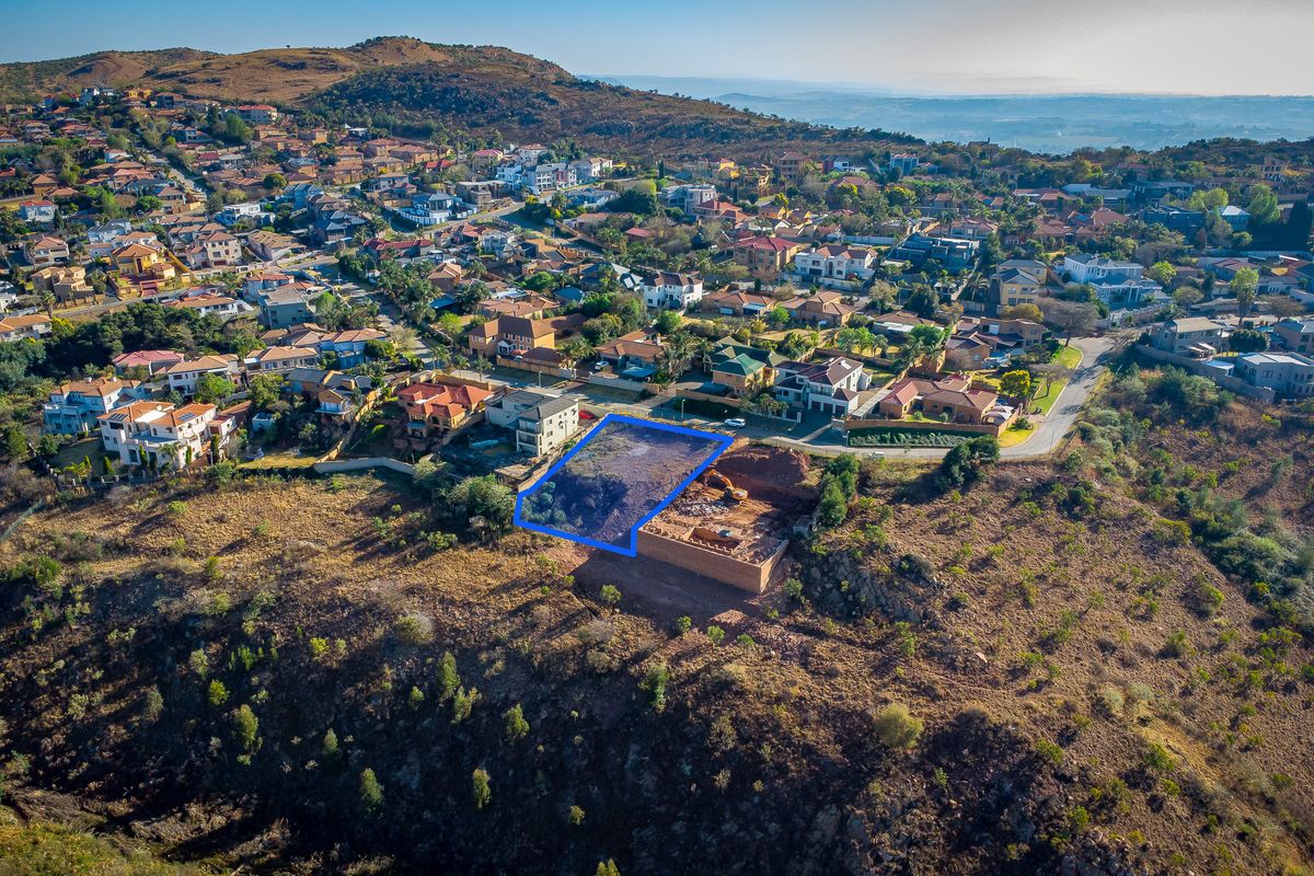 Aerial view of a vacant residential plot featuring a retaining wall and excavation work, situated in a developed hillside neighborhood.