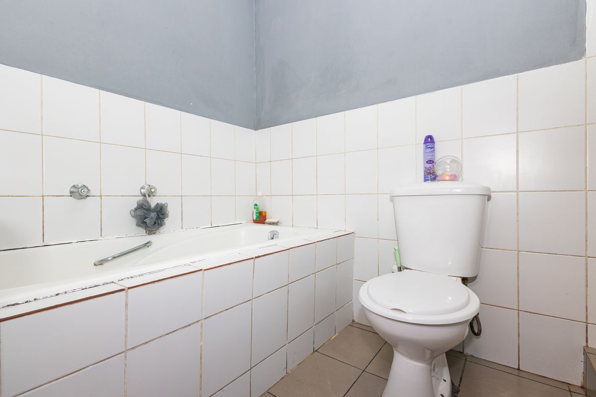 A functional bathroom featuring a built-in bathtub and standard toilet, finished with white wall tiles and grey painted upper walls.