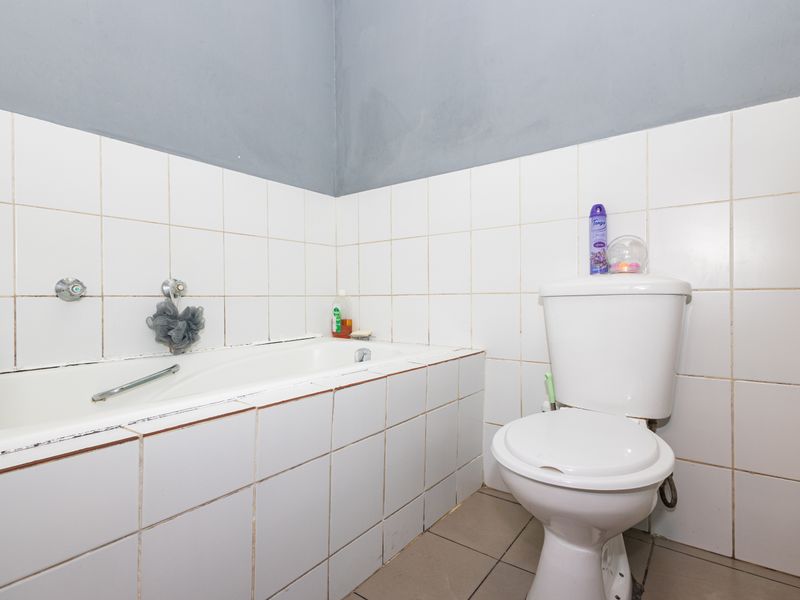 A functional bathroom featuring a built-in bathtub and standard toilet, finished with white wall tiles and grey painted upper walls.