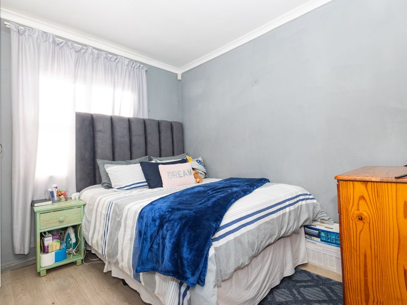 A compact bedroom featuring laminate flooring and neutral grey walls, providing a functional space ready for personalization.