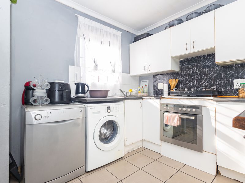 Compact kitchen featuring white built-in cabinetry, marble-effect splashback, built-in oven, gas hob, and tiled flooring.