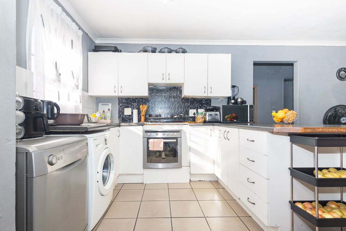 A functional kitchen featuring white cabinetry, a marble-look splashback, built-in oven, gas hob, and tiled flooring with integrated laundry appliance space.