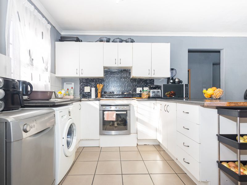 A functional kitchen featuring white cabinetry, a marble-look splashback, built-in oven, gas hob, and tiled flooring with integrated laundry appliance space.