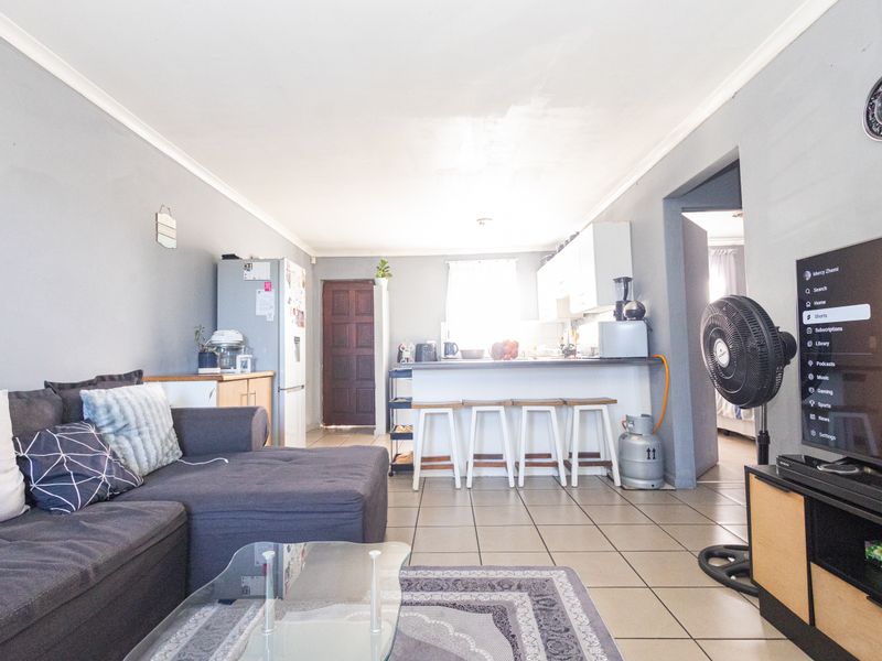 Open-plan living and kitchen area featuring tiled flooring, neutral wall tones, and a functional kitchen layout with breakfast bar seating.