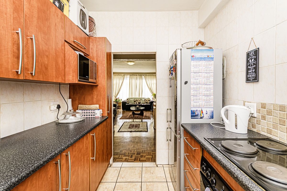 A functional galley-style kitchen featuring wood-look cabinetry, dark countertops, and tiled finishes, with a direct view into the adjacent living area.