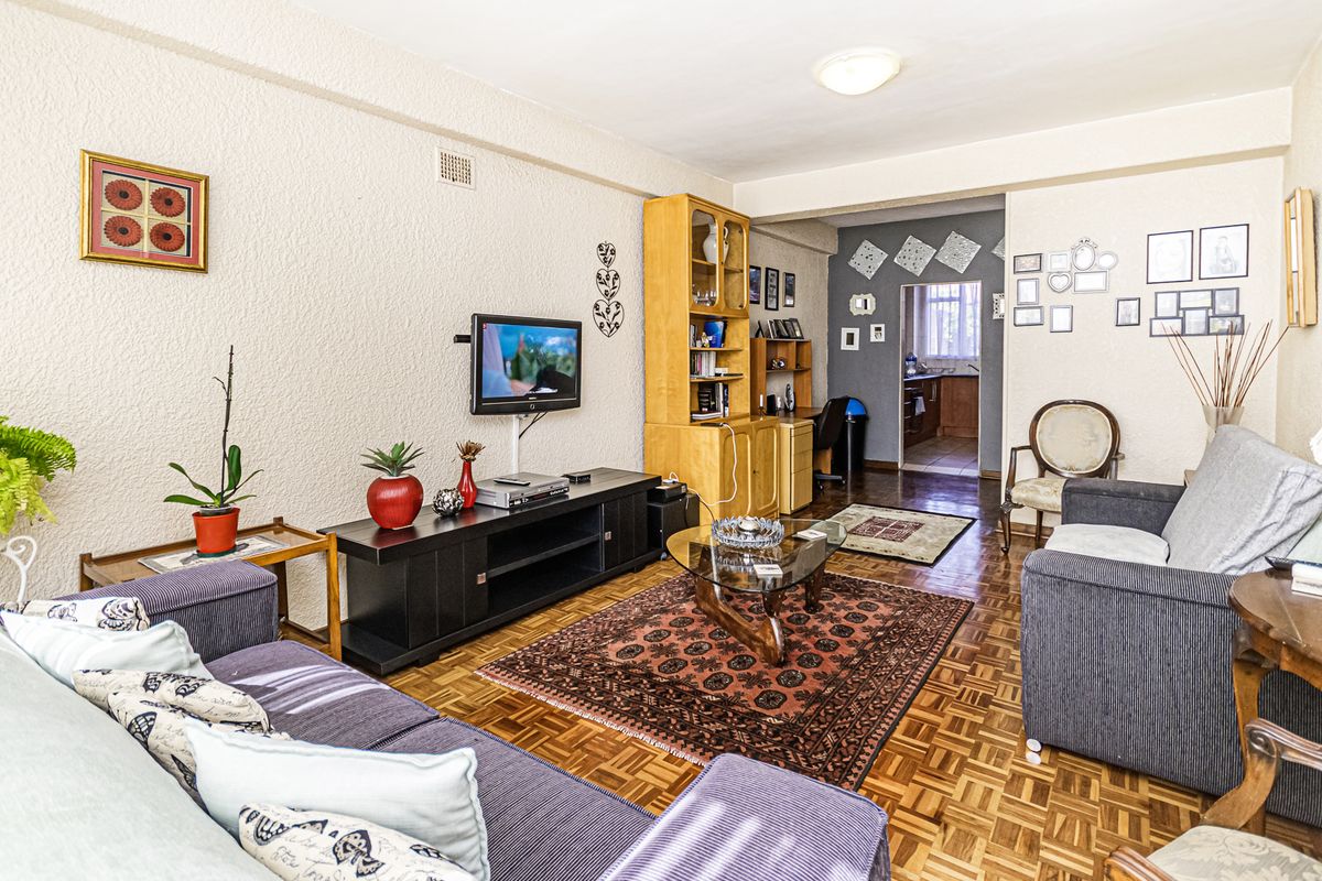 A living room featuring classic parquet flooring and textured walls, with an open transition leading to the kitchen area.