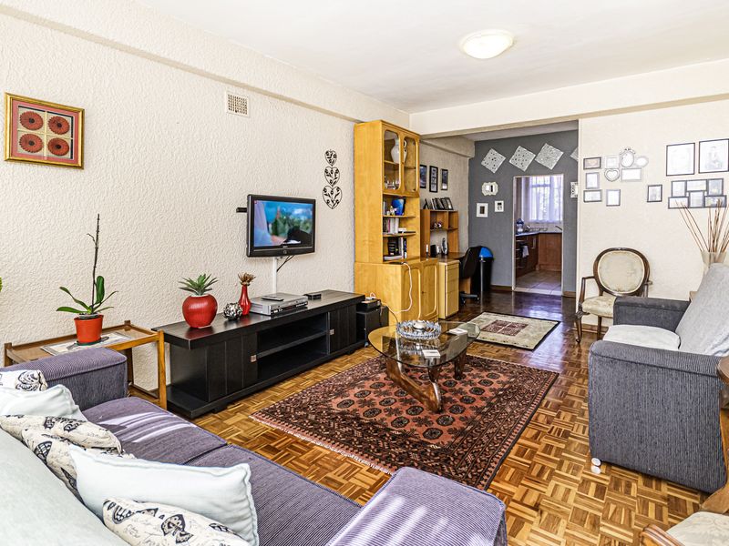 A living room featuring classic parquet flooring and textured walls, with an open transition leading to the kitchen area.