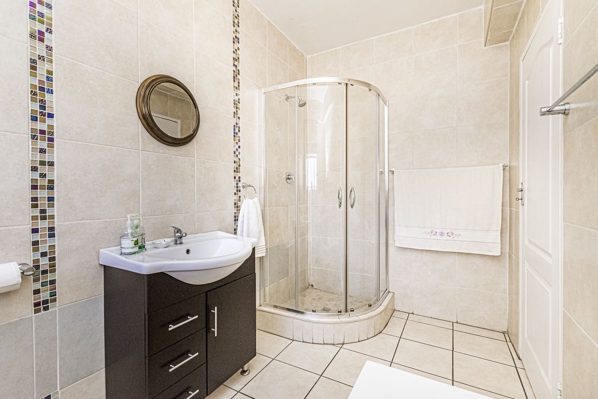 A well-maintained bathroom featuring a corner shower enclosure, a modern vanity cabinet with a basin, and neutral wall tiles with decorative mosaic accents.