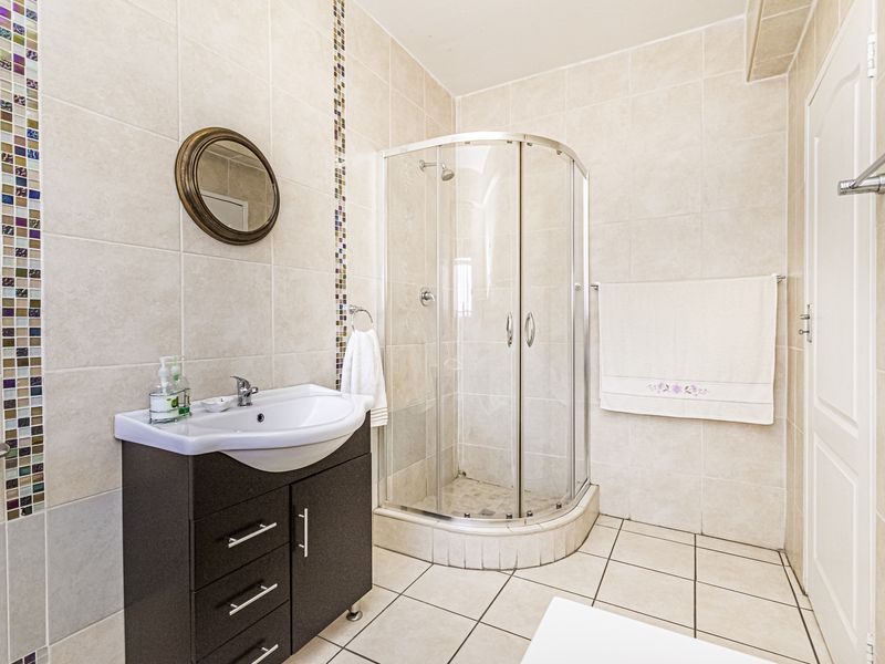 A well-maintained bathroom featuring a corner shower enclosure, a modern vanity cabinet with a basin, and neutral wall tiles with decorative mosaic accents.
