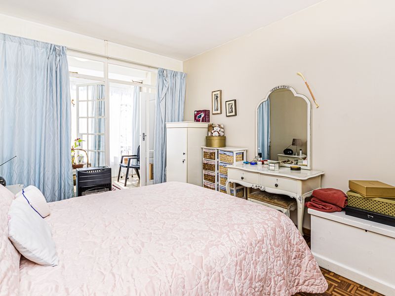 A well-lit bedroom featuring classic parquet flooring and direct access to an adjoining balcony through traditional French doors.