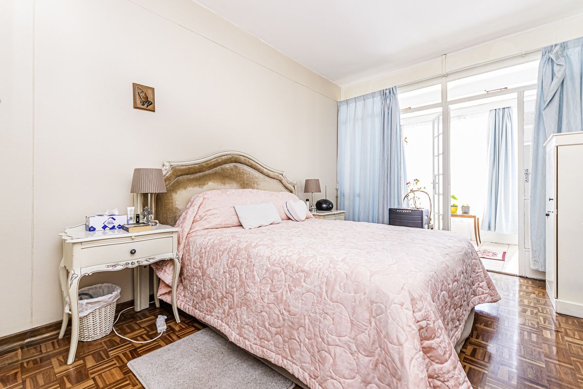 A bedroom featuring classic parquet flooring and direct access to an adjoining balcony through glass sliding doors.