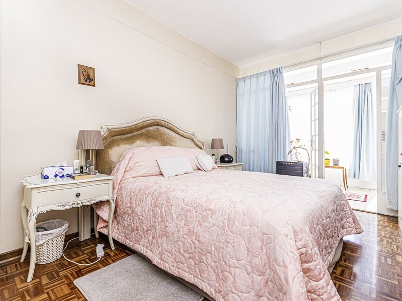 A bedroom featuring classic parquet flooring and direct access to an adjoining balcony through glass sliding doors.