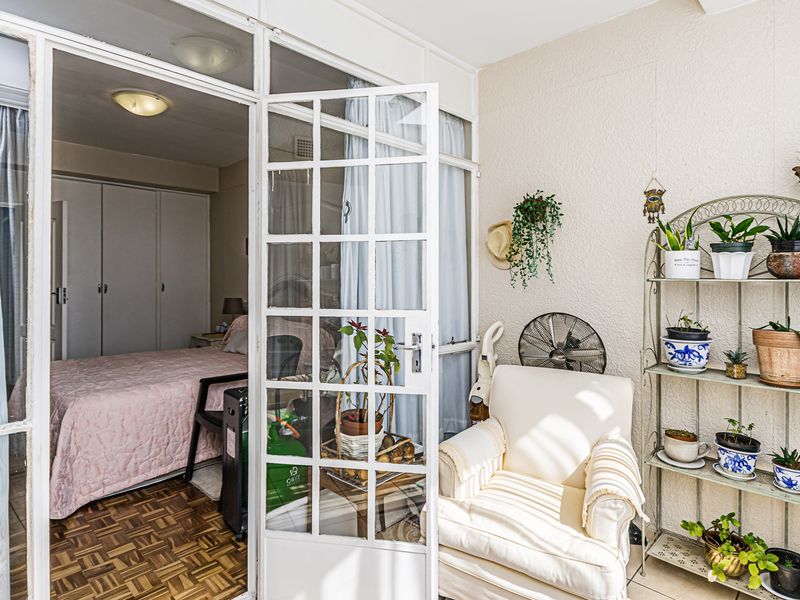 A covered balcony area featuring white-framed french doors leading into a bedroom with parquet flooring and built-in cupboards.