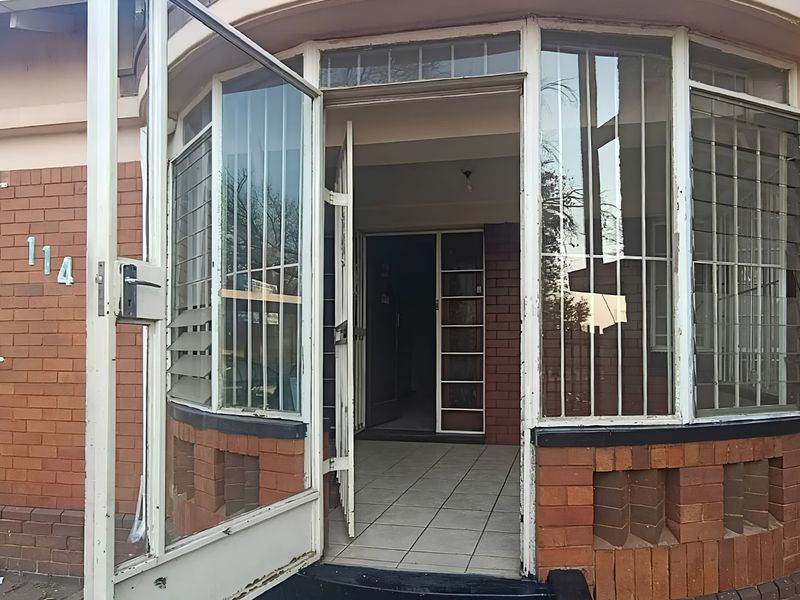 Front entrance of a brick house featuring a tiled porch, metal security door, and window security bars.