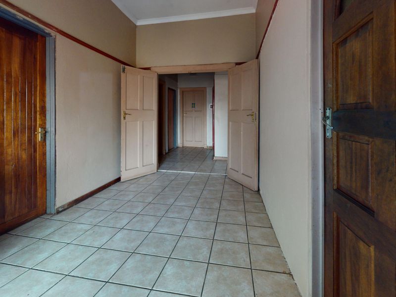 A spacious, empty hallway featuring tiled flooring and multiple wooden panel doors, providing access to various rooms within the home.